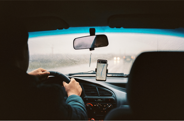 a person driving a car in the rain and using the navigation map displayed on their cell phone