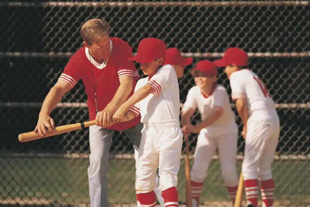 A youth baseball coach helping a young player, with three other players in the background