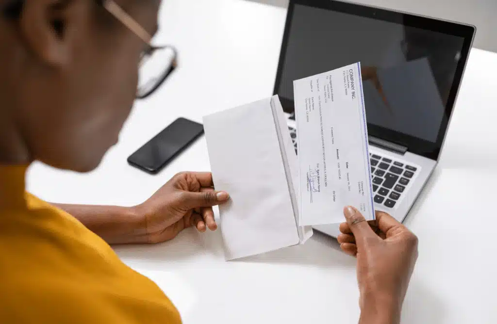 An employee opening a check with a laptop and phone on the table