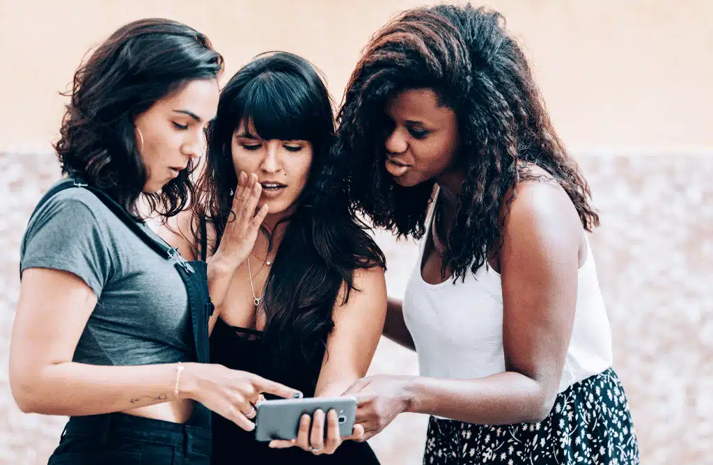 Three young women huddled together and looking at a smartphone