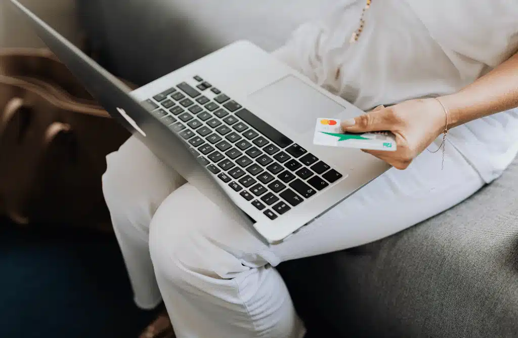 a person sitting with a laptop on their lap and holding a debit or credit card