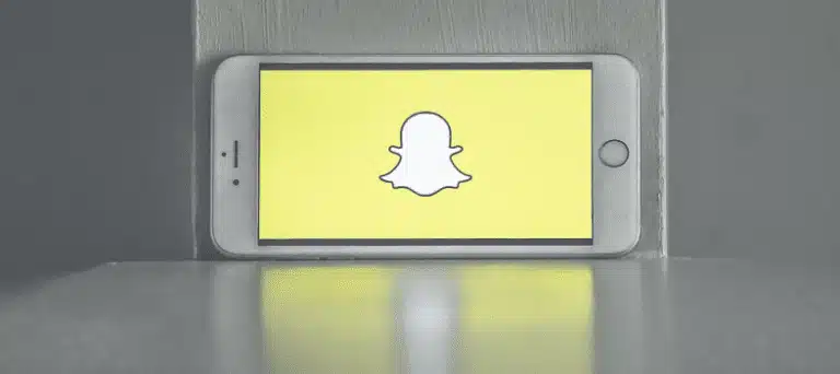 A smartphone propped up on its side against a wall displaying the snapchat app logo