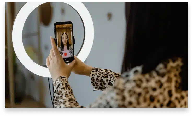 A rear view shot of a person holding up a smartphone attached to a ring light and recording a video for tiktok