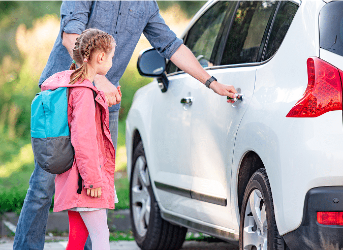 An adult trying to open the back door of a white car while holding a little girl's hand