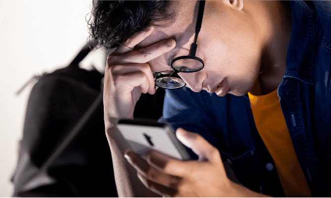 Closeup of a young man leaning forward with his hands on his forehead, looking down at his phone