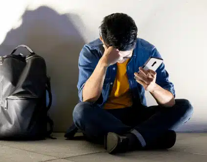 a distressed looking man sitting on the floor after being cyberbullied