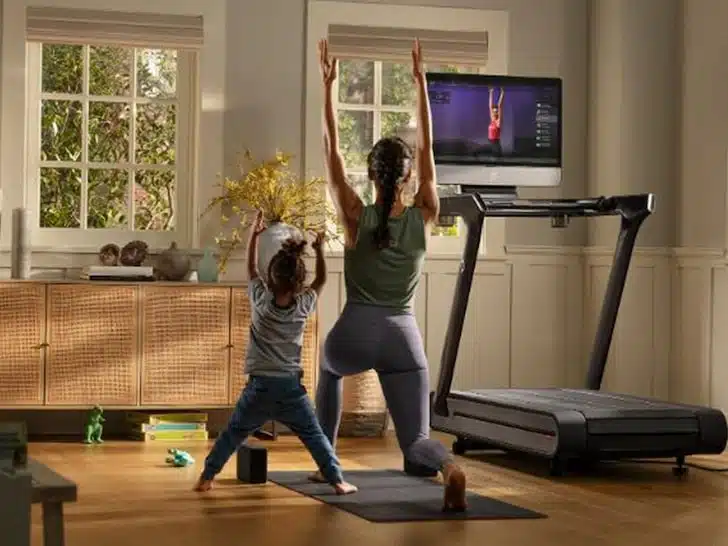 Woman and child stretching next to a Peloton