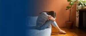 A distressed woman sitting on the edge of a bed with her head resting on her knees