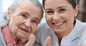 A close-up image of an elderly woman and a nurse smiling at the camera