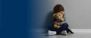 A child sitting on the floor hugging a teddy bear