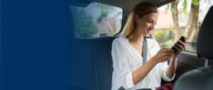 A woman sitting in the back seat of a car looking down at her cell phone