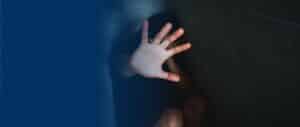 A closeup of a person crouched down, raising one hand with their palm facing forward in a stop or defensive gesture