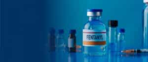 A closeup of a bottle labeled "FENTANYL" with other bottles in the background and a syringe
