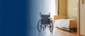 A wheelchair next to an empty bed in a nursing home